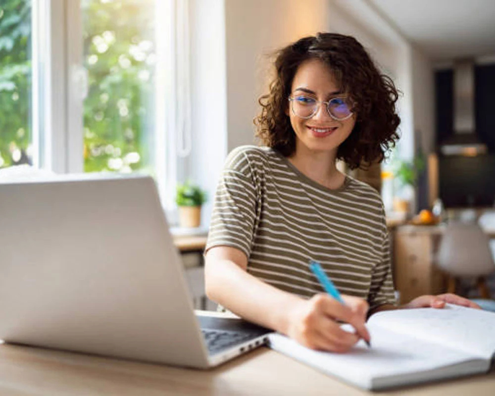 Girl at a laptop writing on a piece of paper
